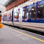 woman in orange coat walking beside train at the station